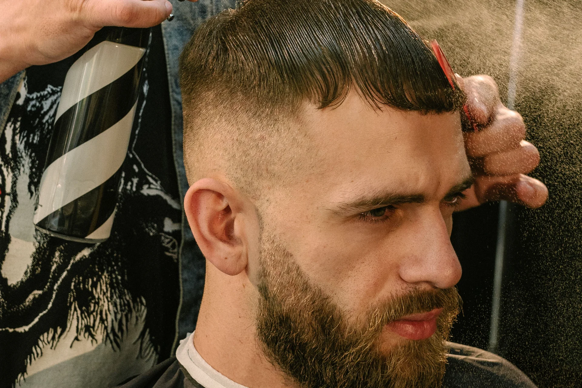 Fryzura edgar męska: przewodnik po modnym cięciu i stylizacji 1 Brodaty mężczyzna siedzi na fotelu fryzjerskim, fryzjer strzyże jego włosy maszynką.