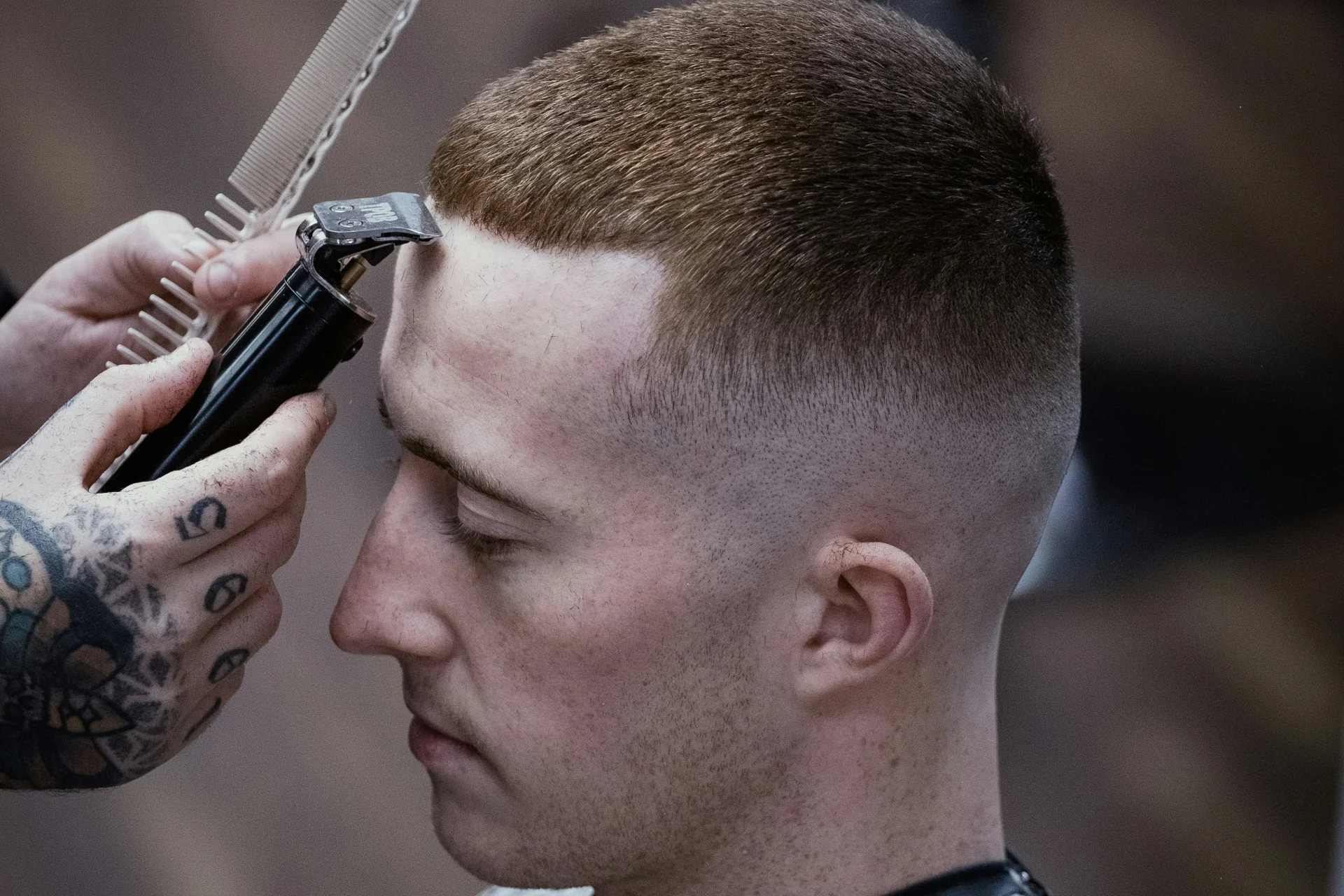 Fryzura edgar męska: przewodnik po modnym cięciu i stylizacji 2 Mężczyzna siedzi na krześle, a fryzjer strzyże mu włosy maszynką do strzyżenia.